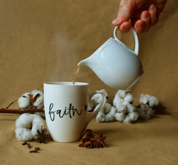 A comforting scene of tea being poured into a faith-themed mug, surrounded by spices and cotton flowers.