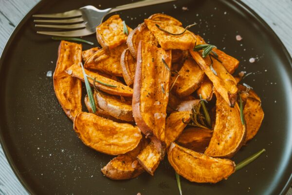 Close-up of crispy sweet potato wedges topped with rosemary, perfect for a healthy snack.