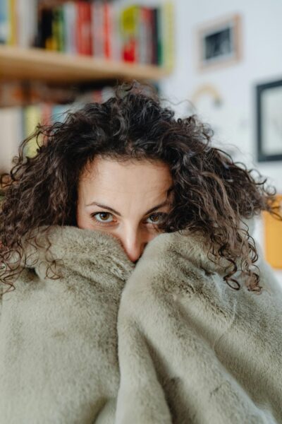 A woman with curly hair warmly wrapped in a cozy fur blanket indoors.