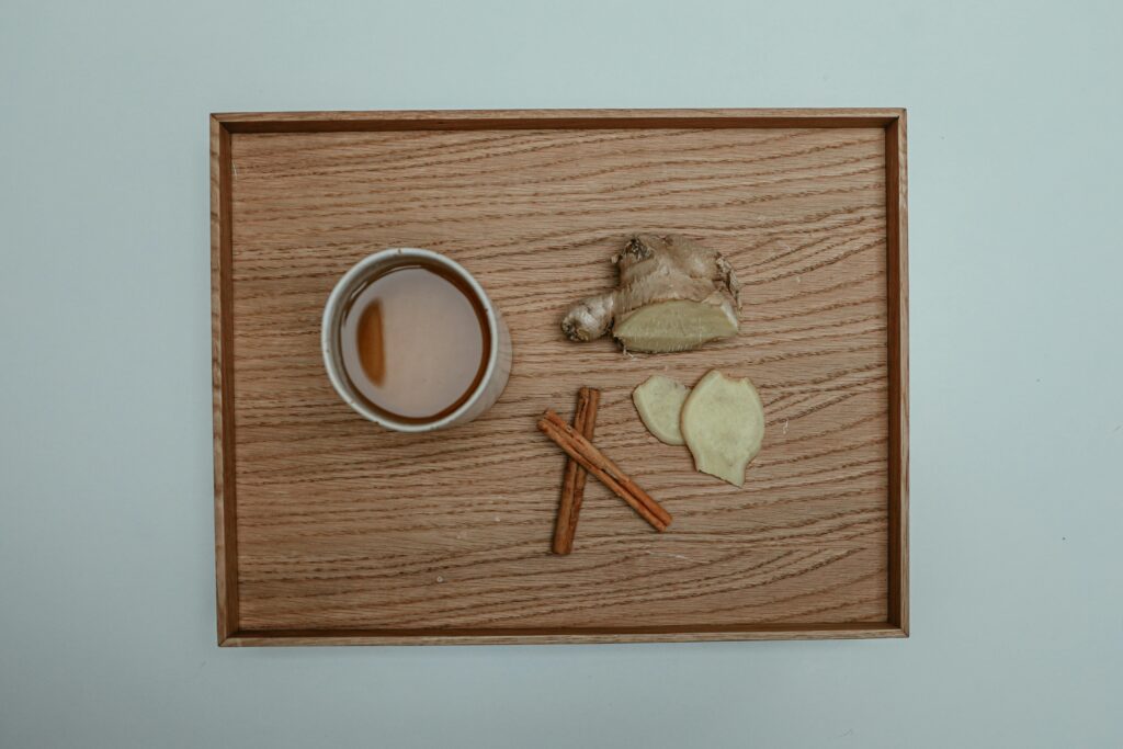 Flat lay image of a cup of tea with cinnamon sticks and fresh ginger on a wooden tray.